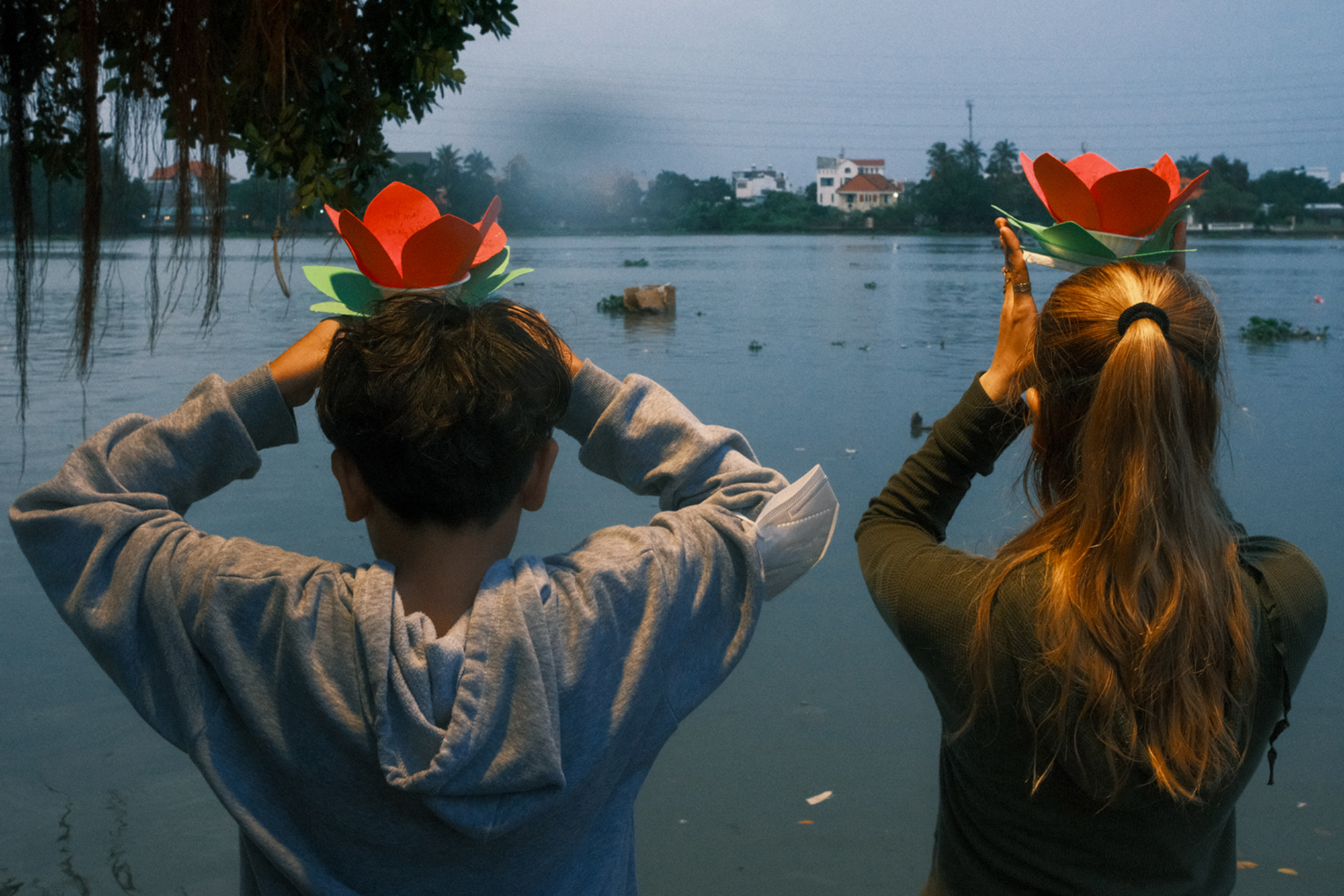 Mother and son pray before placing paper flowers into the river.